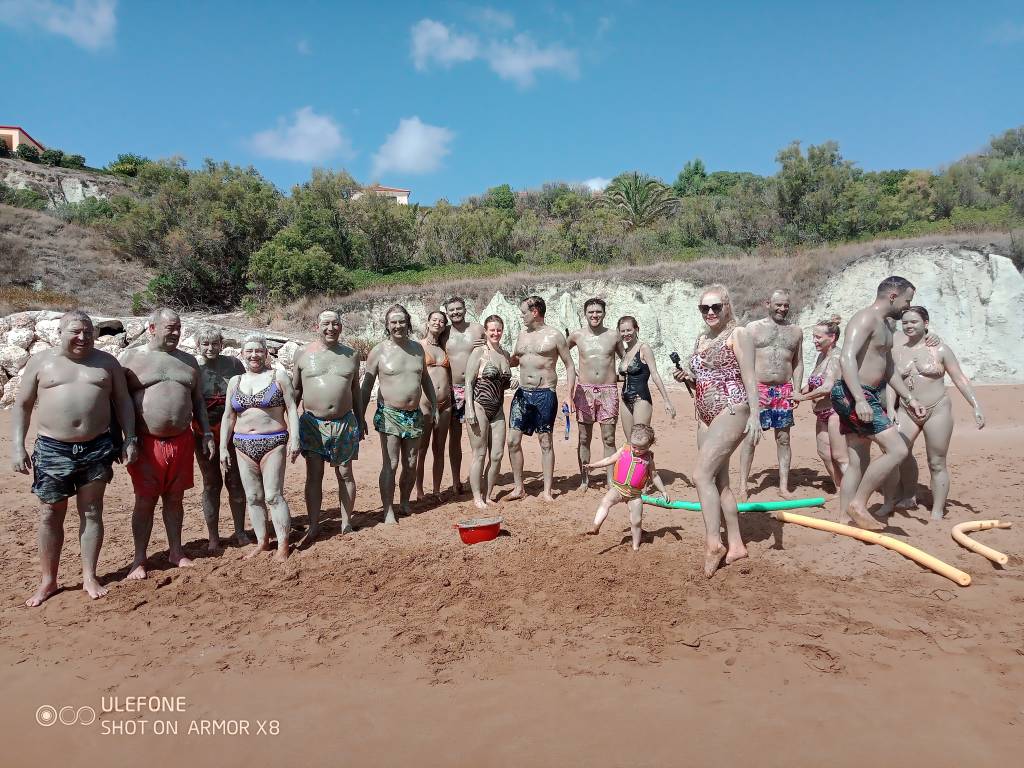 Group of people covered in mud posing on a sandy beach